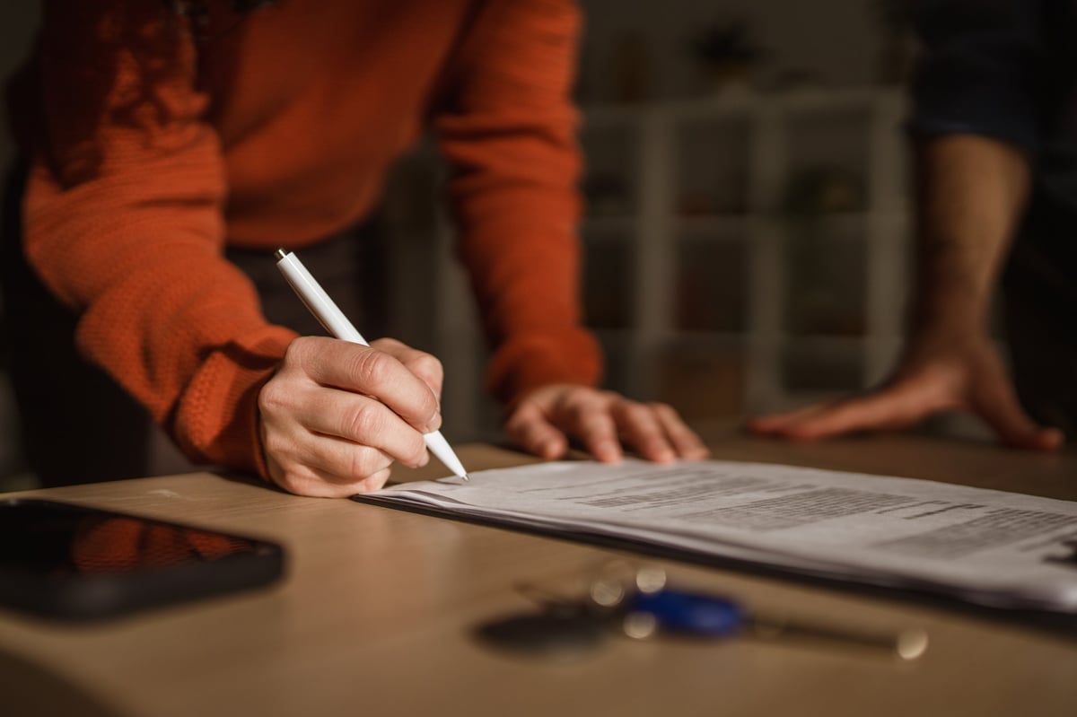 A hand signing a formal document during a property transaction